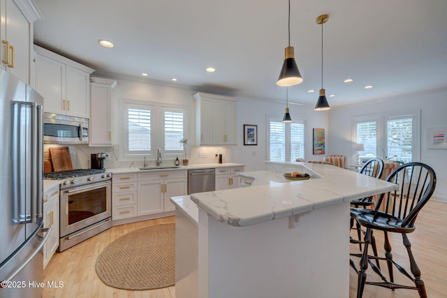 kitchen with appliances with stainless steel finishes, a sink, a center island, a kitchen breakfast bar, and light wood-style floors
