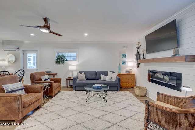 living room featuring wood finished floors, ornamental molding, a glass covered fireplace, an AC wall unit, and a ceiling fan