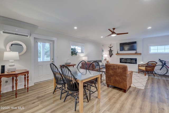 dining space with a wall mounted AC, ornamental molding, light wood-type flooring, healthy amount of natural light, and a fireplace