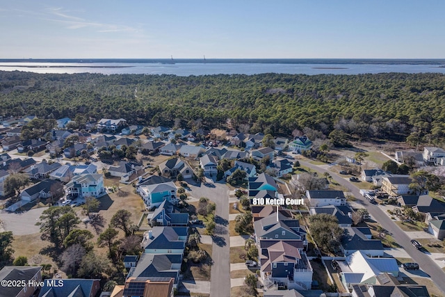 aerial view of property's location featuring nearby suburban area, a large body of water, and a heavily wooded area