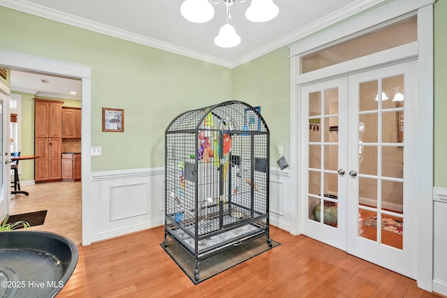 workout area featuring a decorative wall, a wainscoted wall, light wood-style floors, ornamental molding, and french doors