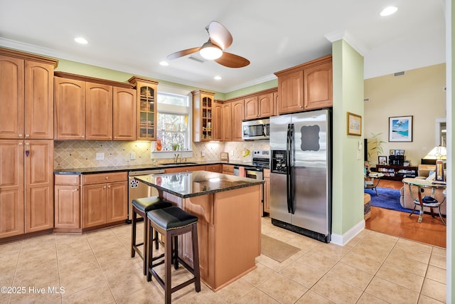 kitchen featuring glass insert cabinets, appliances with stainless steel finishes, dark stone countertops, a kitchen bar, and light tile patterned flooring