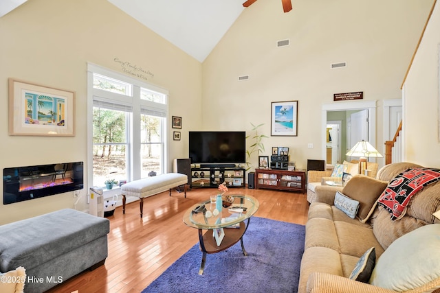 living area featuring high vaulted ceiling, a glass covered fireplace, visible vents, and wood finished floors