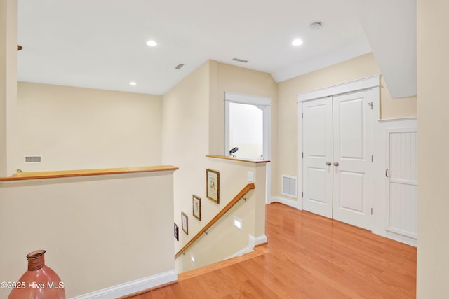 hallway with wood finished floors, an upstairs landing, and visible vents