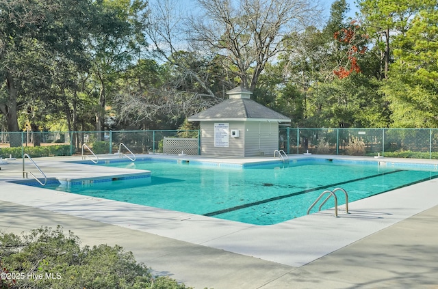 community pool with fence, an outdoor structure, and a patio