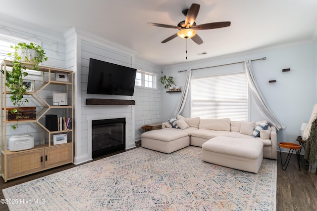 living area with visible vents, ceiling fan, wood finished floors, crown molding, and a fireplace