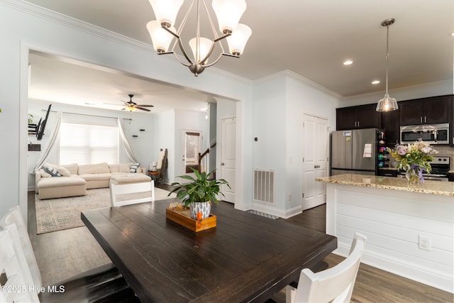 dining room featuring crown molding, dark wood finished floors, visible vents, stairway, and ceiling fan with notable chandelier