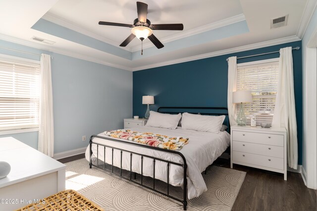 bedroom featuring a tray ceiling, visible vents, baseboards, and wood finished floors