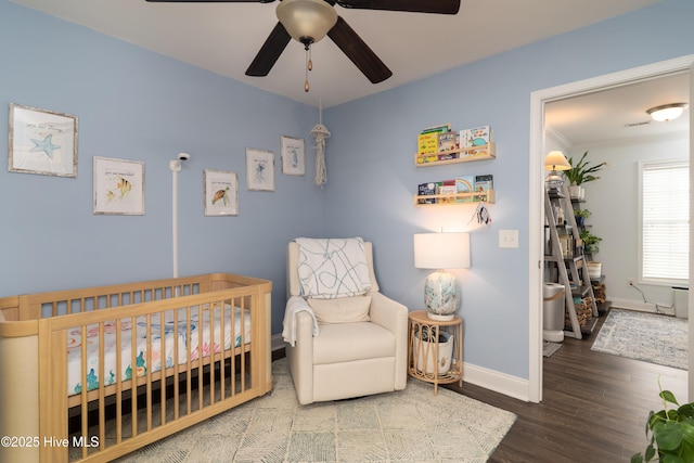 bedroom with a nursery area, ceiling fan, wood finished floors, and baseboards