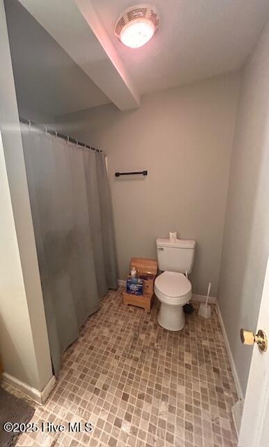 bathroom featuring toilet, curtained shower, and baseboards