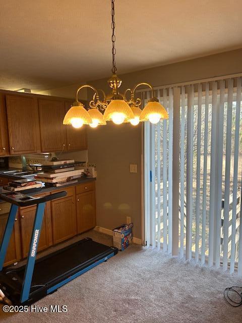 kitchen featuring brown cabinetry, dark countertops, carpet, pendant lighting, and a notable chandelier