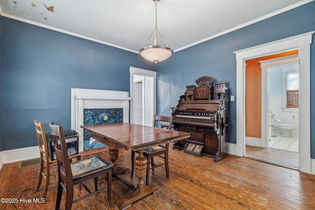 dining space with wood-type flooring, a fireplace, baseboards, and crown molding