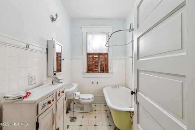 bathroom featuring toilet, a wainscoted wall, a sink, a freestanding tub, and tile walls