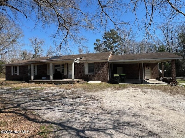 ranch-style home featuring driveway, a porch, an attached carport, and brick siding