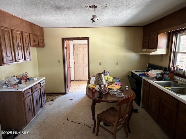 kitchen with a sink, light countertops, a textured ceiling, and range with gas cooktop