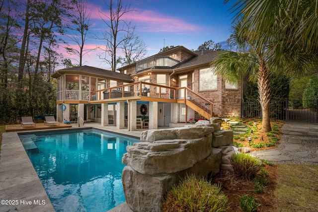 back of house at dusk featuring a patio, a sunroom, a balcony, and stairway
