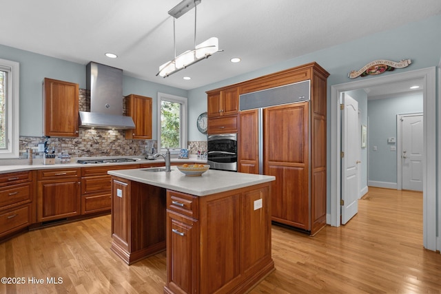 kitchen with wall chimney range hood, paneled built in fridge, brown cabinetry, and stainless steel gas stovetop