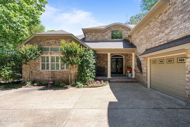 view of exterior entry featuring a porch, roof with shingles, brick siding, and concrete driveway
