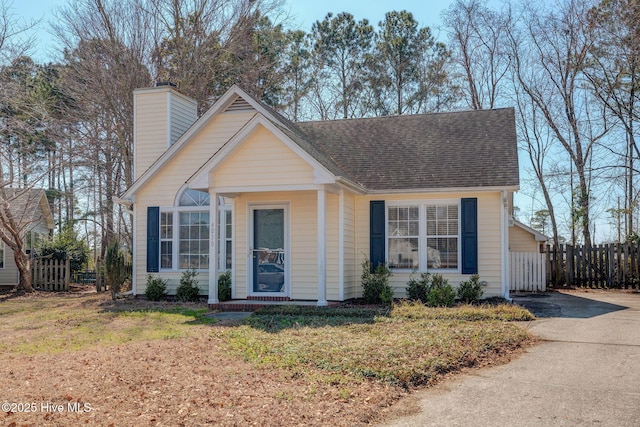 view of front of house featuring roof with shingles, a front lawn, a chimney, and fence