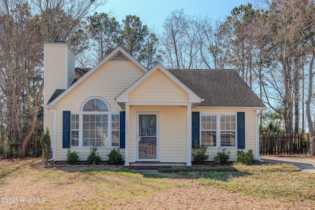 view of front of property featuring a shingled roof, a chimney, a front yard, and fence