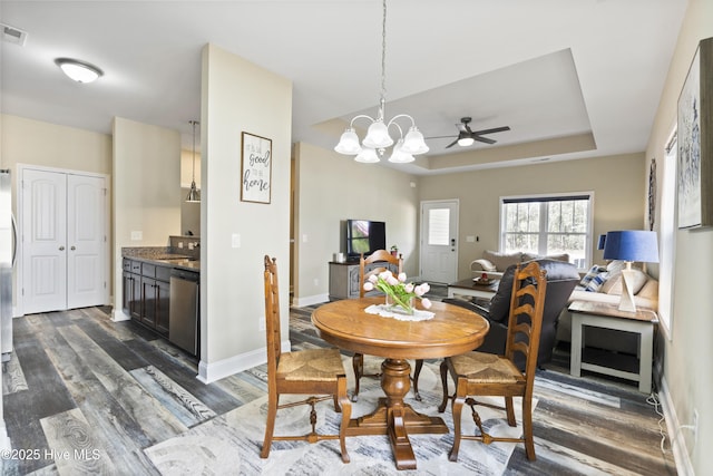 dining room with baseboards, visible vents, dark wood finished floors, a tray ceiling, and ceiling fan with notable chandelier