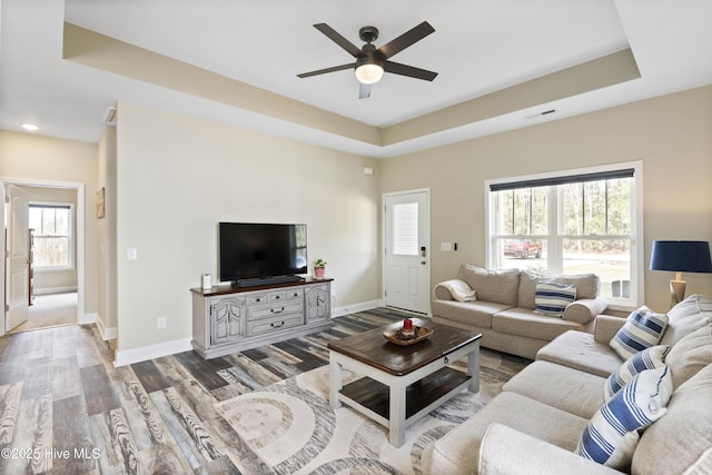 living area featuring visible vents, baseboards, wood finished floors, a raised ceiling, and a ceiling fan