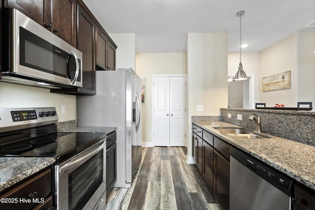 kitchen with dark brown cabinetry, light stone countertops, stainless steel appliances, and a sink