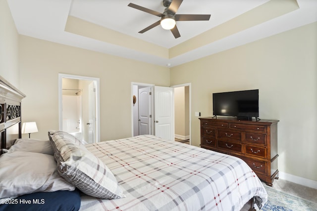 bedroom with carpet, baseboards, ensuite bath, ceiling fan, and a raised ceiling