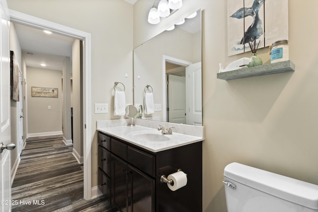 half bathroom with toilet, vanity, baseboards, and wood finished floors