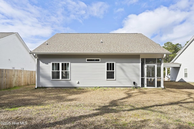 rear view of house with a lawn, fence, roof with shingles, and a sunroom