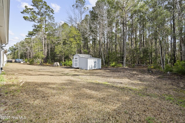 view of yard with a storage unit, a view of trees, and an outdoor structure