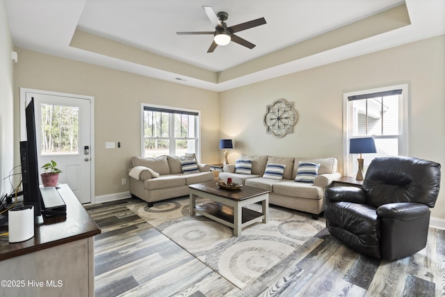 living area featuring a tray ceiling, plenty of natural light, baseboards, and wood finished floors