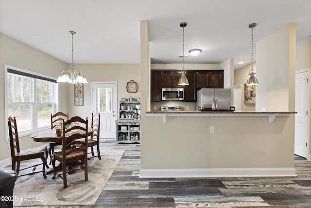 kitchen with wood finished floors, baseboards, stone countertops, stainless steel appliances, and dark brown cabinetry