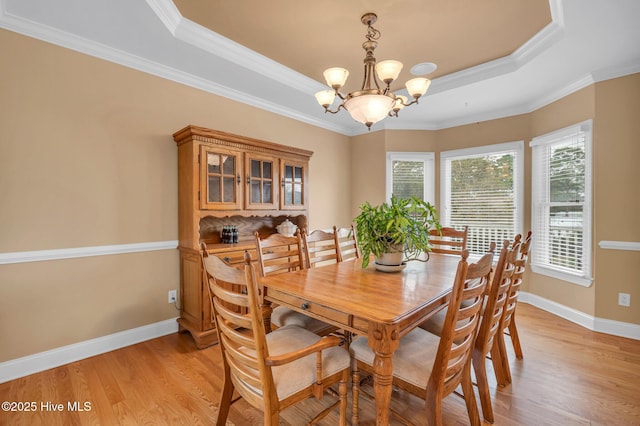 dining area with baseboards, ornamental molding, a raised ceiling, light wood-type flooring, and a chandelier