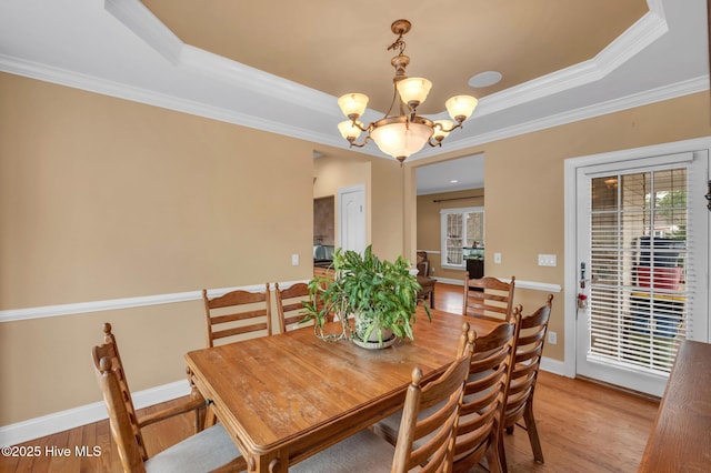 dining room featuring ornamental molding, a tray ceiling, light wood-style floors, baseboards, and a chandelier