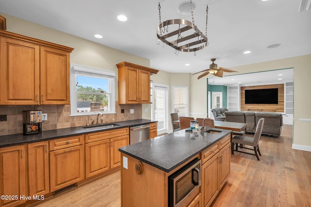 kitchen with stainless steel appliances, a sink, a kitchen island with sink, backsplash, and light wood-style flooring