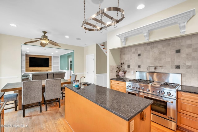kitchen featuring high end stove, a kitchen island with sink, light wood-style flooring, a sink, and a ceiling fan