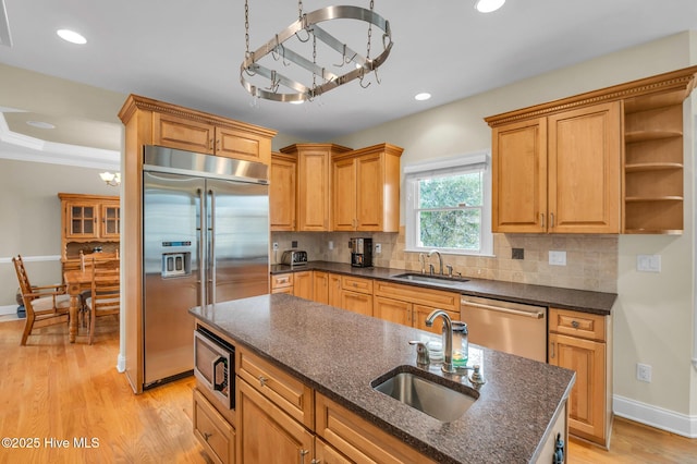 kitchen with light wood finished floors, tasteful backsplash, built in appliances, and a sink