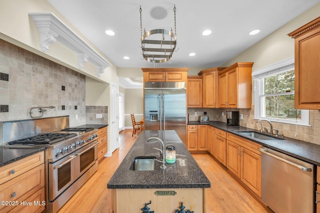 kitchen featuring premium appliances, light wood-style flooring, an island with sink, and a sink