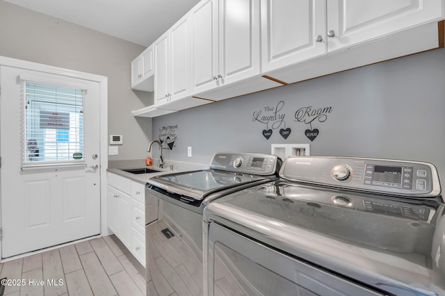 clothes washing area featuring washing machine and clothes dryer, wood finish floors, cabinet space, and a sink