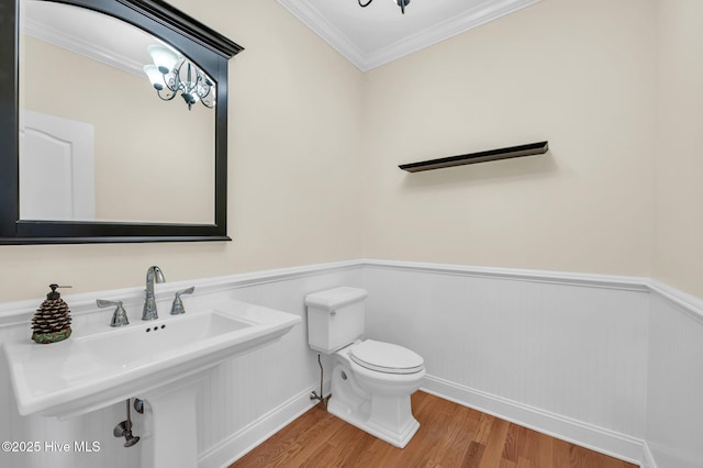 bathroom with crown molding, wood finished floors, a wainscoted wall, and toilet