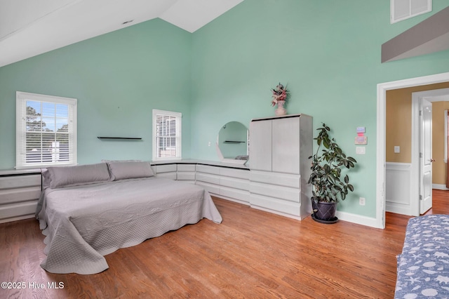 bedroom featuring baseboards, wood finished floors, visible vents, and high vaulted ceiling