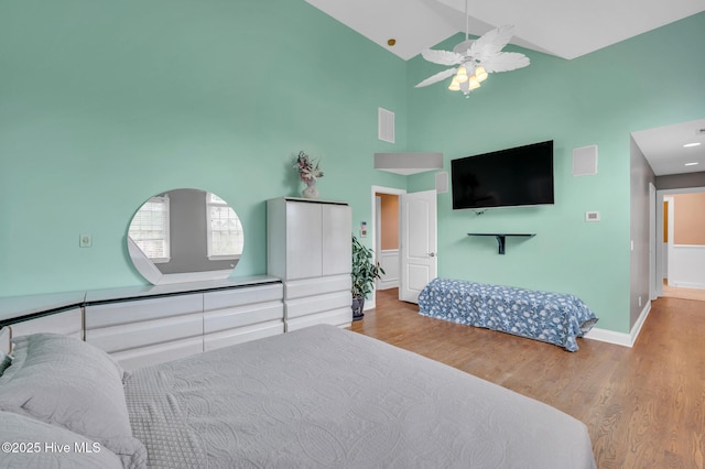 bedroom featuring wood finished floors, visible vents, baseboards, high vaulted ceiling, and ceiling fan