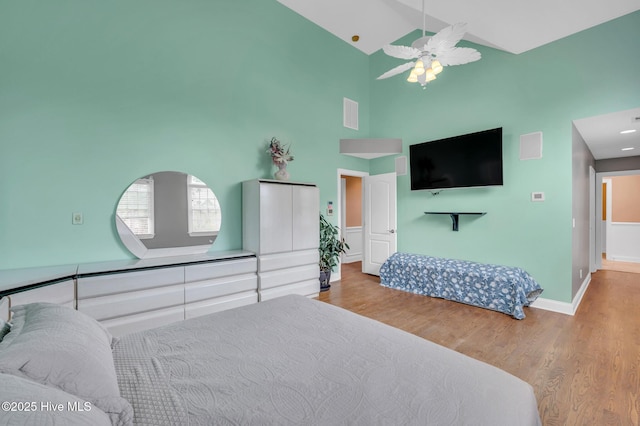 bedroom featuring wood finished floors, high vaulted ceiling, baseboards, and a ceiling fan