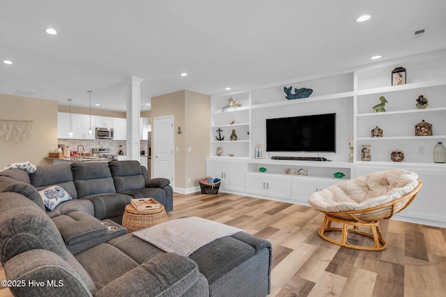 living room featuring light wood-style floors, recessed lighting, baseboards, ornate columns, and built in shelves