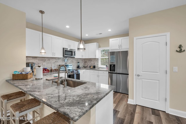 kitchen featuring stone counters, a peninsula, decorative backsplash, white cabinets, and appliances with stainless steel finishes