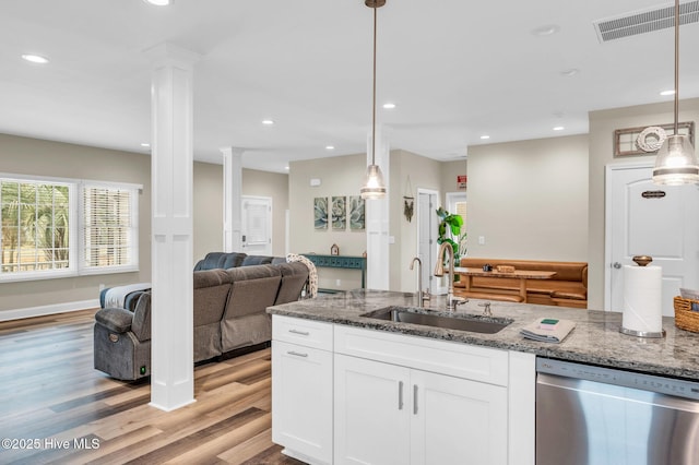 kitchen featuring stainless steel dishwasher, a sink, ornate columns, light wood-style floors, and white cabinetry