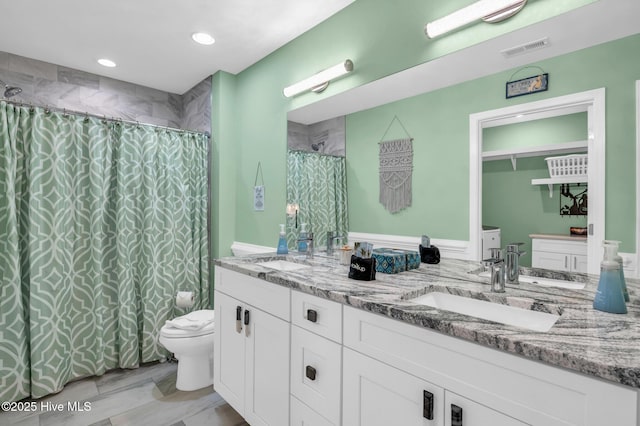 bathroom featuring double vanity, visible vents, toilet, and a sink