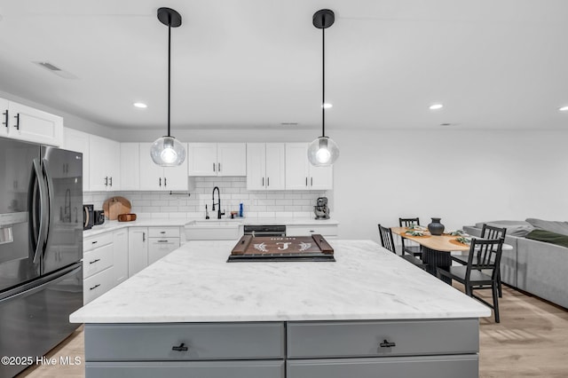 kitchen featuring gray cabinetry, a sink, backsplash, black fridge with ice dispenser, and a center island