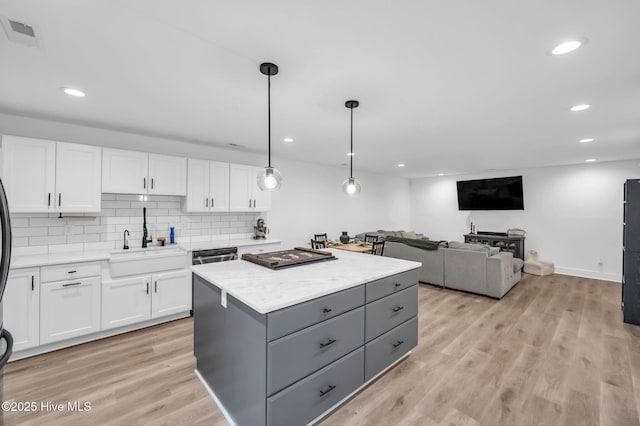 kitchen featuring a sink, gray cabinetry, white cabinetry, a center island, and light countertops